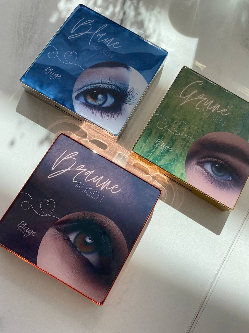 Drei Lidschattenpaletten von Kluge Beauty für blaue, grüne und braune Augen, stilvoll arrangiert mit individuellen Farbschemata.