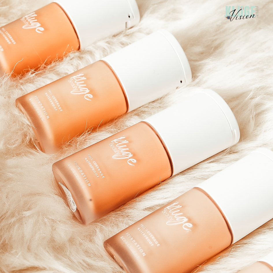 Kluge Beauty Foundation-Flakons in einer Reihe auf weichem, cremefarbenem Fell präsentiert. Die Flaschen zeigen eine luxuriöse Verpackung mit minimalistischen weißen Kappen.