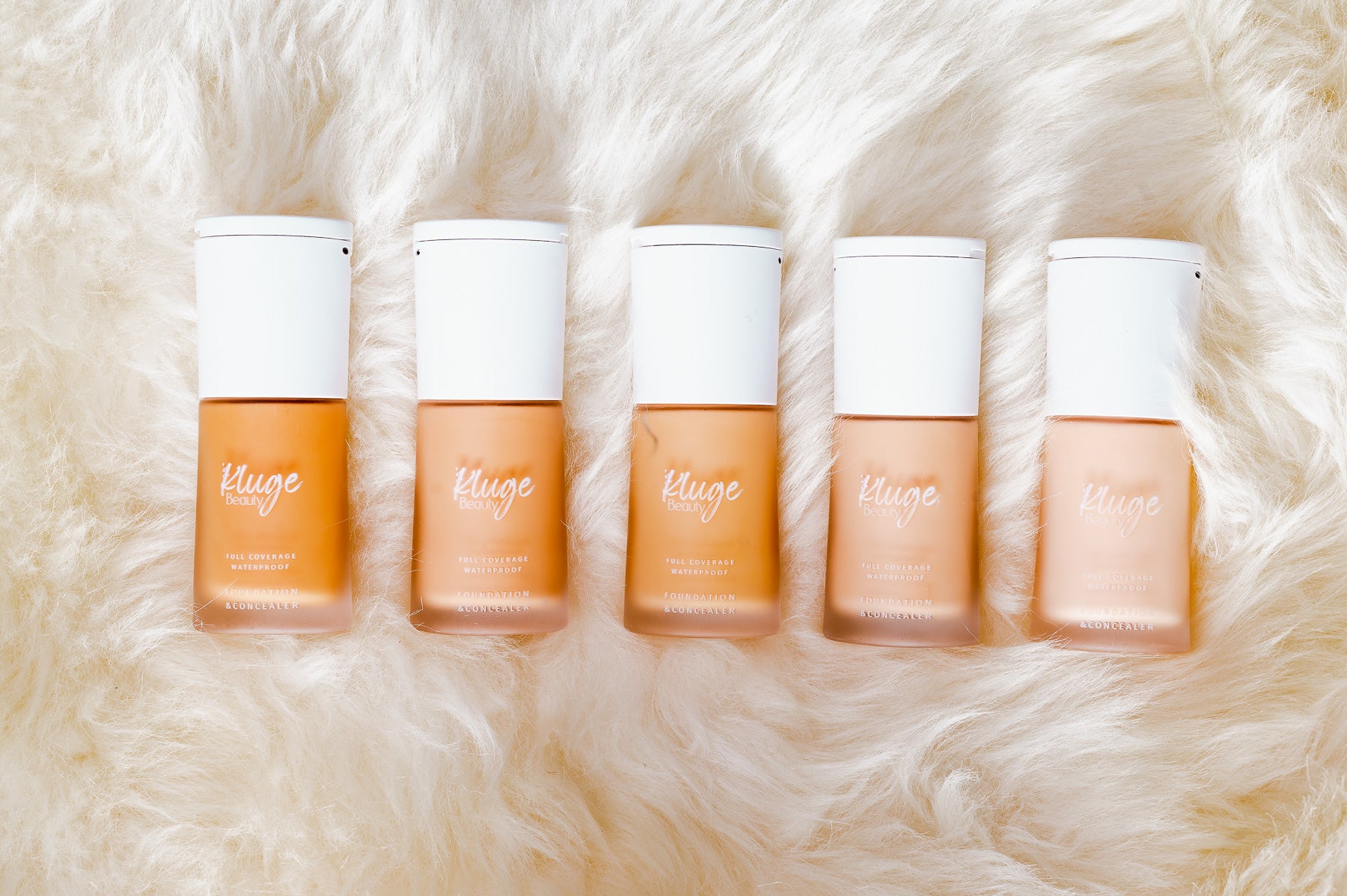 Fünf verschiedene Farbtöne der Kluge Beauty Foundation elegant auf weichem Fell arrangiert, ideal zur Darstellung von Farbvielfalt.