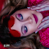 Kreatives Porträt einer Frau mit pinkem Augen-Make-up, knallpinkem Lippenstift und einer herzförmigen Brille, vor einem lebhaften Hintergrund.