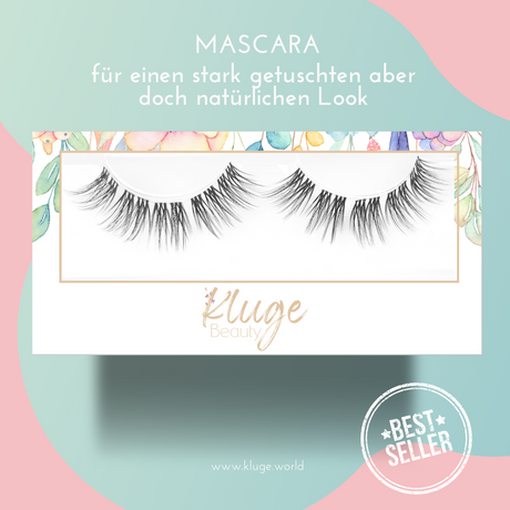 Nahaufnahme einer luxuriösen Wimpernbox mit "Mascara" für einen intensiven, dennoch natürlichen Look, präsentiert auf einem stilvollen pastellfarbenen Hintergrund.