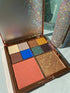 Offene Lidschattenpalette von Kluge Beauty mit kräftigen Blau-, Grün- und Goldtönen, kombiniert mit Rouge.