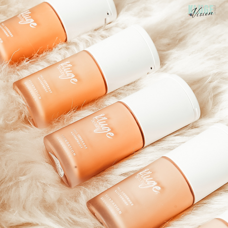 Kluge Beauty Foundation-Flakons in einer Reihe auf weichem, cremefarbenem Fell präsentiert. Die Flaschen zeigen eine luxuriöse Verpackung mit minimalistischen weißen Kappen.